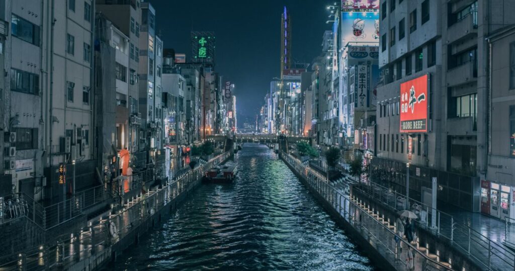 導入文 日本には多様な方言が存在しますが、その中でも特に人々を惹きつけるのが関西弁です。独特のイントネーションや豊かな表現力、そしてお笑い文化と深く結びついたユーモラスな言葉遣いは、全国的に親しまれています。本記事では、そんな関西弁の中でも近年注目を集める「生きとったんかワレ」という表現に焦点を当て、その意味や使われ方、文化的な背景について詳しく解説していきます。 関西弁の魅力とは? 関西弁とは何か?その特色を知ろう 関西弁は、大阪や京都、兵庫、奈良、滋賀、和歌山など関西地方一帯で広く使われる方言で、親しみやすくユーモラスな響きを持っています。標準語と比べてもイントネーションの抑揚が大きく、独特のリズムやアクセントが特徴的です。例えば「ほんま」「せやな」「ちゃうねん」といった言い回しは、相手に柔らかく、時には力強くメッセージを伝える役割を果たします。こうした独自性から全国的にも人気が高く、テレビやラジオ、さらにお笑い文化を通じて広く浸透し、関西弁を耳にするだけで明るく楽しい雰囲気をイメージする人も少なくありません。さらに、最近ではSNSや動画配信を通じて若い世代にも支持を集め、日常会話にちょっとしたスパイスを加える表現として親しまれています。 関西弁の歴史と文化的背景 関西弁は古くから京都を中心に発展してきました。京都は長らく都であったため、公家や武家の言葉遣いに影響を受けつつも、庶民の生活に根付いた独自の表現が育まれていきました。特に大阪は商人の町として発展し、取引や交渉の場面で機知に富んだやり取りが重視されました。その結果、洒落や皮肉を込めた表現が数多く生まれ、現代の「ボケとツッコミ」の文化にもつながっています。また、落語や漫才といった伝統芸能を通して関西弁は全国に広まり、親しみやすく、時に鋭い言葉遣いとして定着しました。今日でもテレビ番組や舞台芸能では欠かせない要素となっており、関西弁そのものがエンターテインメントの一部と見なされています。 関西弁のコミュニケーション能力について 関西弁は、相手との距離を縮める効果が非常に高いと言われています。日常会話では自然に笑いやツッコミが入りやすく、会話がリズミカルに展開されるため、相手との心理的距離を一気に縮めることができます。例えば初対面の相手でも「どないやねん」「なんでやねん」といったフレーズを交えることで、場の空気が柔らかくなり、堅苦しさを和らげます。また、ユーモアを交えたやり取りが相手に安心感を与え、親しみやすい雰囲気を作り出すため、コミュニケーションを円滑にする強力な武器となります。さらに、感情表現の幅が広いため、怒りや喜び、驚きなどをより生き生きと伝えられるのも大きな魅力です。 「生きとったんかワレ」の意味 「生きとったんかワレ」の語源と成り立ち 「生きとったんかワレ」は直訳すると「まだ生きていたのか、お前」という意味になります。関西弁特有の砕けた言い回しで、驚きや懐かしさを強調する表現です。元来は親しい間柄での軽い冗談として使われ、再会の喜びをコミカルに伝える言葉でした。近年はネット掲示板「なんJ」などで頻繁に使われ、ネットスラングとして広まった背景があります。さらにYouTubeやSNSでの配信文化が拡大したことで、若い世代の間でもミーム的に用いられるようになり、関西弁を知らない人にまで定着しています。語源的には「生きていたのか」と「ワレ(お前)」を組み合わせたシンプルな構造ですが、イントネーションや言い方によってニュアンスが大きく変化する点が特徴です。 使われるシチュエーションを深掘り 主に久しぶりに再会した相手に対して冗談めかして使われます。例えば長期間連絡がなかった友人に出会った時、「お前、まだ生きとったんかワレ!」と声をかけることで、再会の喜びや親しさをユーモラスに表現します。時には飲み会や同窓会の席で、笑いを誘う一言として飛び出すこともあります。真剣に言うのではなく、あくまで軽妙なトーンで使うのがポイントで、相手との関係性が近しいほど効果的に働きます。また、SNSやチャット上でも「久々の投稿」に対してコメントする形で用いられることがあり、文字だけでも親しさを演出できる便利なフレーズです。 対話における「生きとったんかワレ」の役割 このフレーズは、相手を笑わせたり、会話を盛り上げたりする役割を担います。単なる驚きの言葉ではなく、相手を大切に思う気持ちや再会の喜びをユーモアに包んで伝えるための表現です。相手を否定するのではなく、むしろ関係性の深さを表すユーモアとして用いられます。親しみの証としての冗談であり、気心の知れた関係だからこそ成立するやり取りです。 「生きとったんかワレ」の具体例 人気のスタンプや素材をチェック LINEスタンプやSNSの素材として「生きとったんかワレ」は人気を集めています。コミカルなイラストと組み合わされることで、気軽に使えるジョーク表現として親しまれています。特にLINEスタンプでは、関西弁特有のイントネーションを文字と表情豊かなキャラクターで表現することで、メッセージのやり取りがさらに楽しくなると好評です。SNSでは画像やGIFアニメとともに投稿されることも多く、見る人の笑いを誘う定番ネタの一つになっています。TwitterやInstagramでも「#生きとったんかワレ」といったハッシュタグが使われ、ユーザー同士のちょっとした冗談や再会の報告に添えられるケースが増えています。 「生きとったんかワレ」を用いた漫画の紹介 関西弁キャラクターが登場する漫画やギャグ作品では、このフレーズが効果的に用いられることがあります。キャラクター同士の掛け合いを強調するための決まり文句としても定番です。特にギャグ漫画では、久々に登場したキャラクターへのツッコミとして読者の笑いを誘う役割を果たしています。また、同人誌や二次創作の世界でもネタ的に使用されることが多く、関西弁の雰囲気を盛り上げるアイテムの一つとなっています。こうした描写は、読者にキャラクター同士の距離感や親しみを直感的に伝える効果があります。 なんJでの使用例を学ぶ ネット掲示板「なんJ」では、スレッドに久々に現れたユーザーや意外な話題に対して「生きとったんかワレ!」と書き込むのが定番。ネット文化の中で愛される表現となっています。さらに、スレッドが過去の話題を蒸し返した際にも、このフレーズで茶化すことで場を和ませることがあります。短いながらもユーモラスな言葉であるため、ネット上での共感や一体感を生み出す要素となり、コミュニティ文化を象徴するフレーズとして位置付けられています。 類似表現や関連表現 「生きとったんかワレ」に似た関西弁の表現 「なんや、まだおったんか」や「元気にしとったんか」なども似たニュアンスを持っています。いずれも久しぶりの再会を冗談めかして表す表現です。さらに「おお、忘れてへんかったで!」や「ほんま久しぶりやなあ」など、驚きと懐かしさを同時に伝える関西弁のフレーズも多く存在します。特に親しい友人同士では「どこ行っとったんや」「死んだんかと思ったわ」といった少し大げさな表現が好まれ、再会の場を笑いに包みます。 反応や返事で使われる他の方言 関西弁以外でも、九州弁の「おっとー、元気やったと?」のように、方言には再会を喜ぶ独自の言い回しがあります。東北弁では「おめ、まだいたのが?」、沖縄弁では「あんた、なま生きとぅたんねー」といった具合に、それぞれの地域文化に根付いた表現が存在します。これらはいずれも驚きと親しみを同時に表すニュアンスを持ち、地域ごとの人柄や気質がにじみ出ています。 方言が持つ独自の意味と文化的意義 方言は地域文化や人間関係の親密さを表す重要な要素です。「生きとったんかワレ」もまた、関西特有の人懐っこさやユーモアを映し出す表現の一つと言えます。方言を用いることで、相手との距離を一気に縮め、会話を温かみのあるものにします。加えて、世代間のつながりを示す文化的な遺産でもあり、親から子へ自然に受け継がれていく言語の財産です。現代においても方言を使うことは、自分のルーツや地域アイデンティティを誇る行為として大きな意味を持っています。 まとめ 「生きとったんかワレ」は、驚きと親しみを込めた関西弁ならではのユーモラスな表現です。もともとは親しい人との軽い冗談として使われてきましたが、近年ではネットスラングとしても広まり、多くの人が気軽に使うフレーズとなっています。その背後には、関西人特有の温かみあるコミュニケーション文化が息づいており、相手を笑わせながら距離を縮める効果が大きいのが特徴です。例えば、久々に再会した友人に使えば場が一気に和み、SNSでコメントすれば親しさを演出できます。このように方言は単なる言葉遣いにとどまらず、文化や人間関係を支える大切な要素として機能しています。方言を通して地域の文化を理解することは、単に言葉を知るだけではなく、その土地の価値観や人々の生き方を感じ取ることでもあります。結果として、より深い人間関係や会話の楽しさを味わえるだけでなく、自分自身のコミュニケーション力を豊かにするきっかけにもなるでしょう。